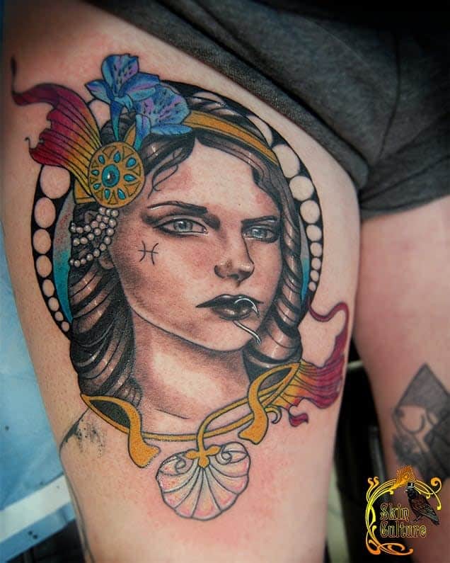 Colorful Art Nouveau tattoo of a woman with detailed jewelry, floral accents, and soft, vibrant tones framed by an ornate design