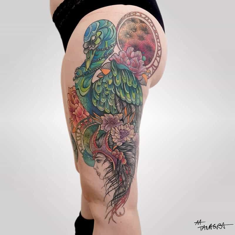 A vibrant Art Nouveau tattoo with a skeletal bird with ornate green feathers, blooming flowers, and a woman in a tribal headdress