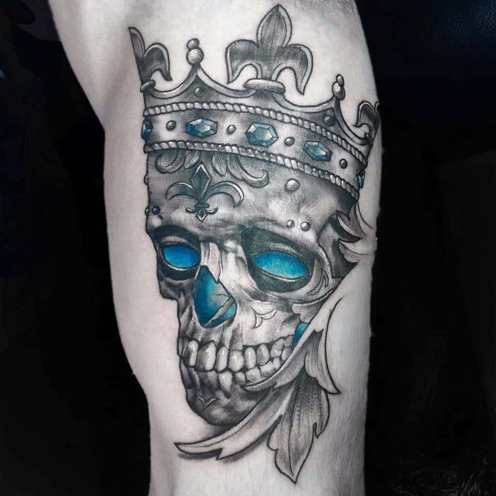 A detailed Art Nouveau-inspired tattoo featuring a crowned skull adorned with blue gemstones and elegant ornamental designs