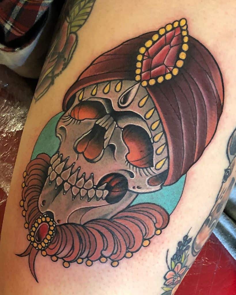 A bold tattoo featuring a regal skull wearing a jeweled turban and intricate collar, blending elegance with macabre artistry