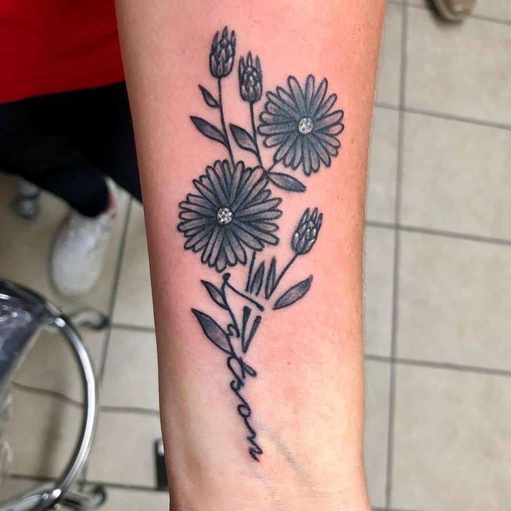 Tattoo of aster flowers with stems forming the word "bloom" on a forearm