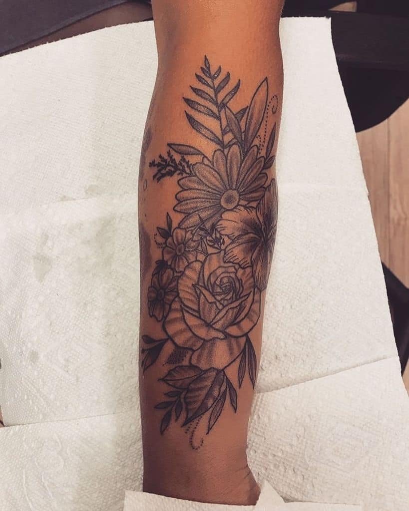 A large floral tattoo on the forearm, showcasing a mix of asters, roses, and lush foliage