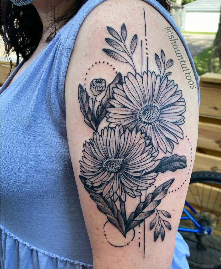 Upper arm tattoo with large daisies, leaves, and an elegant aster in black and gray ink