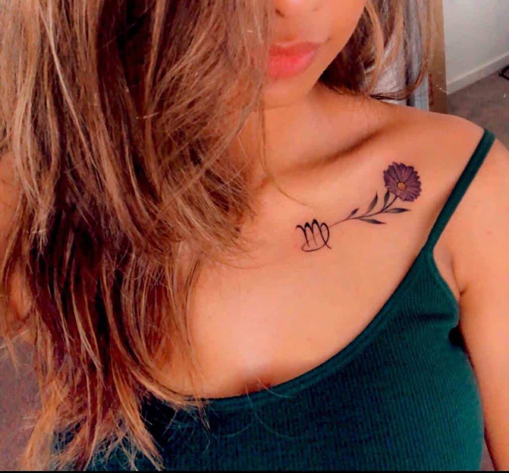 A delicate purple aster tattoo on the collarbone, accompanied by a simple minimalist design