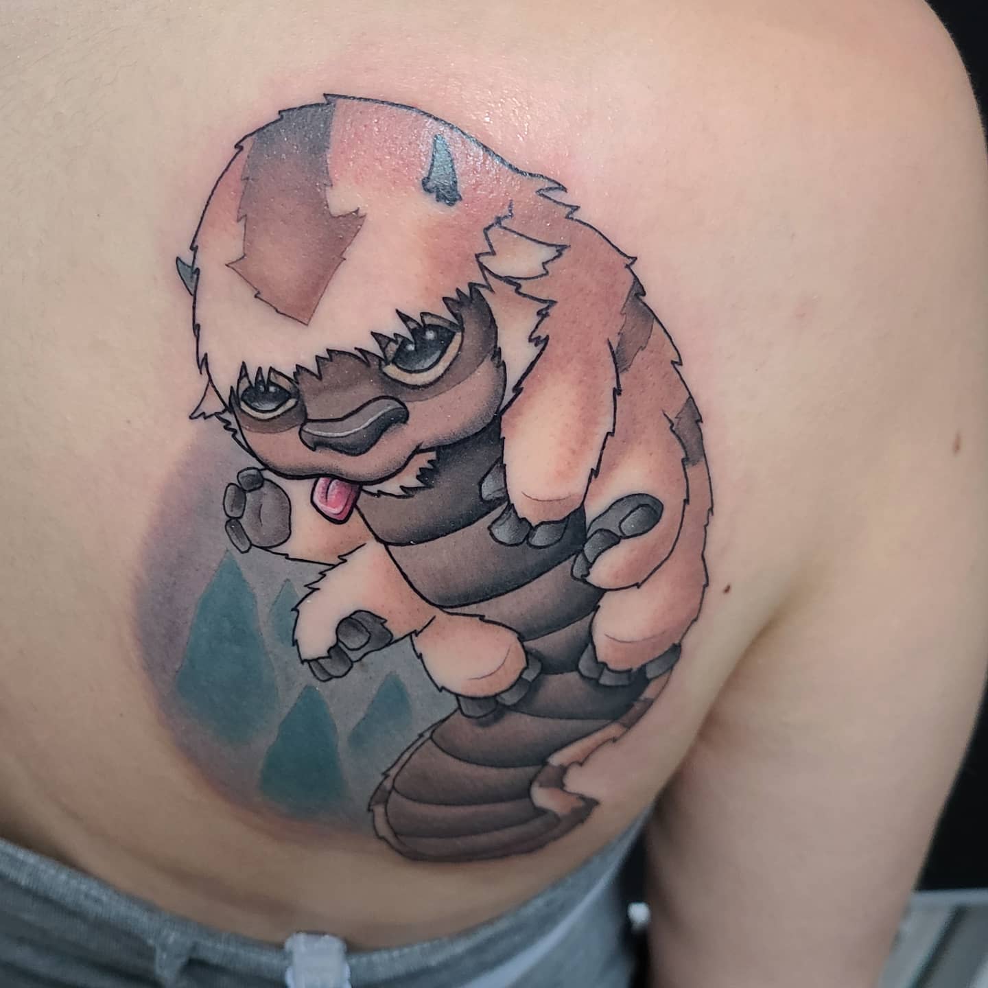 Tattoo of Appa in a cute, chibi-style, flying over mountains on the upper back