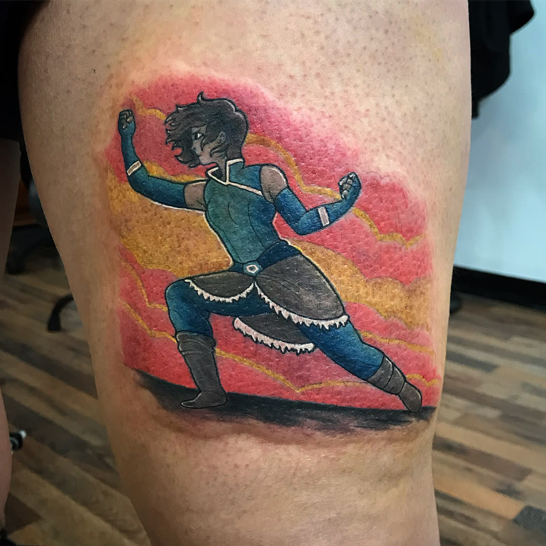 Tattoo of Korra in a fighting stance, with a colorful sunset background on the thigh