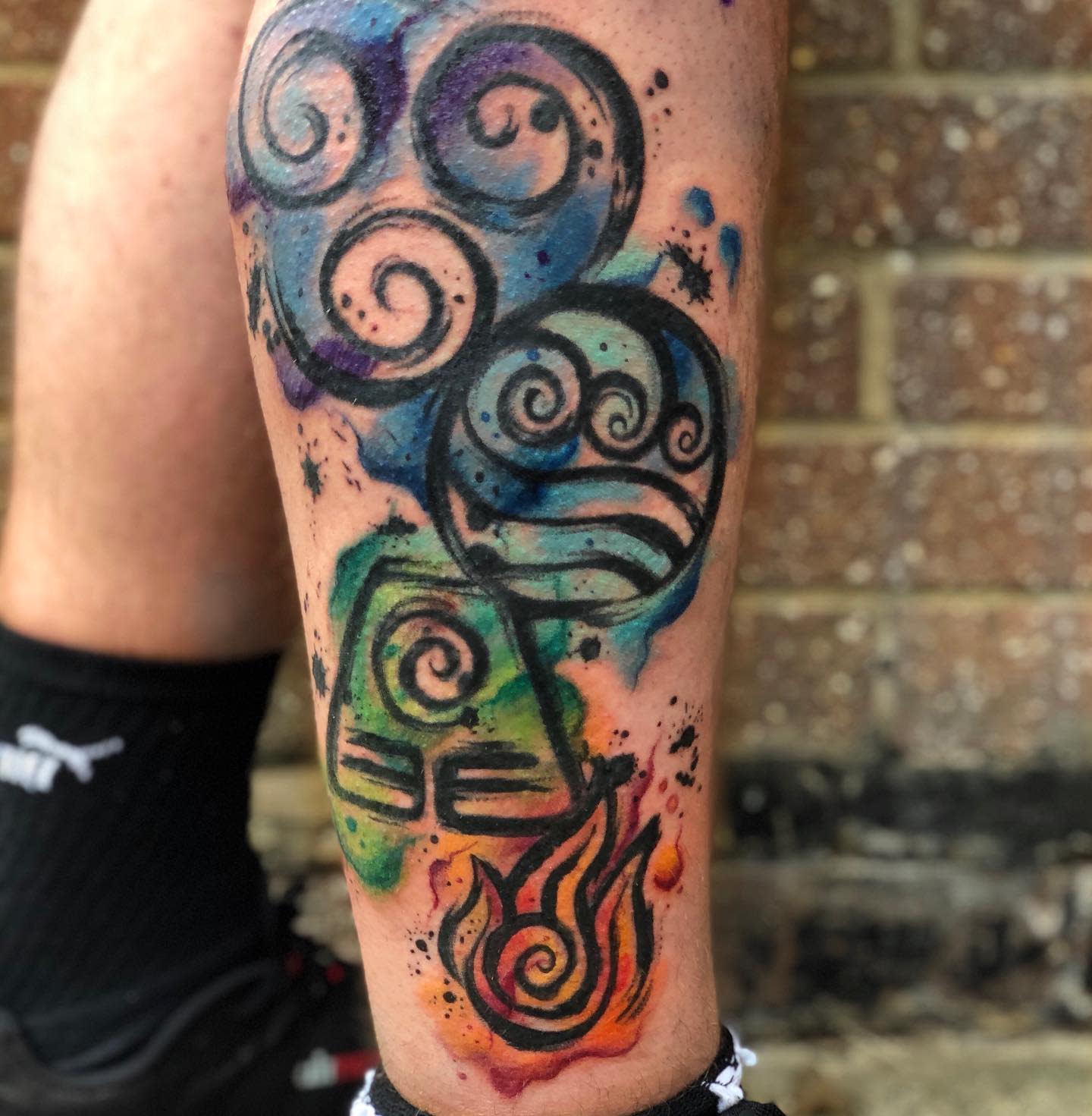 Colorful tattoo of elemental symbols on a leg featuring fire, water, earth, and air icons