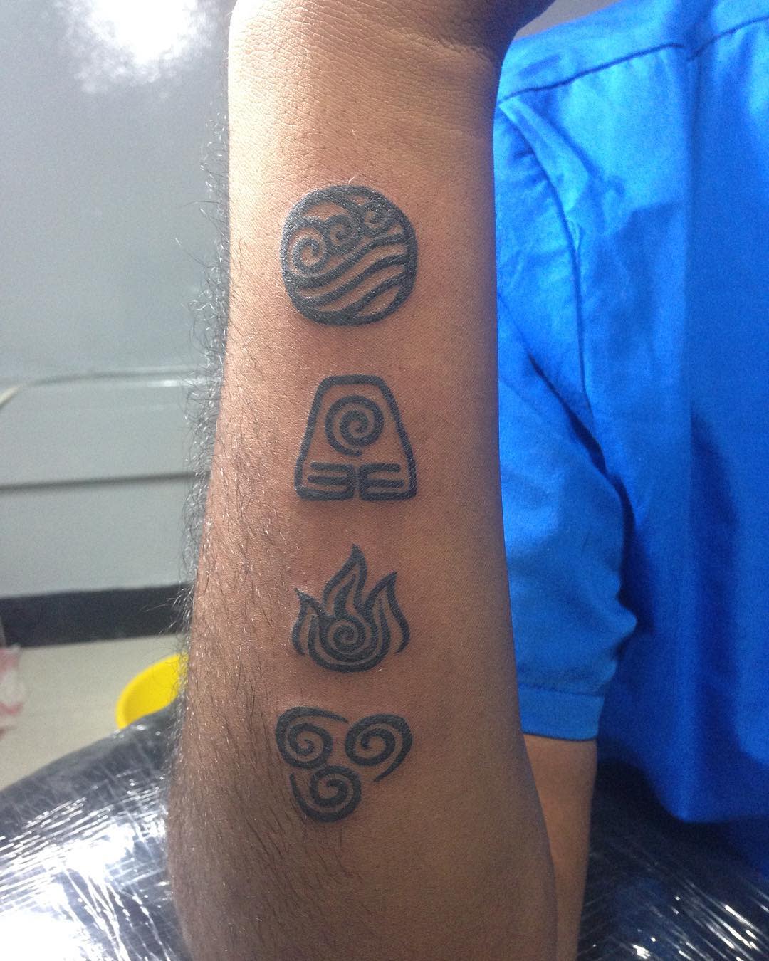 Forearm tattoos of four element symbols: water, earth, fire, and air, in black ink