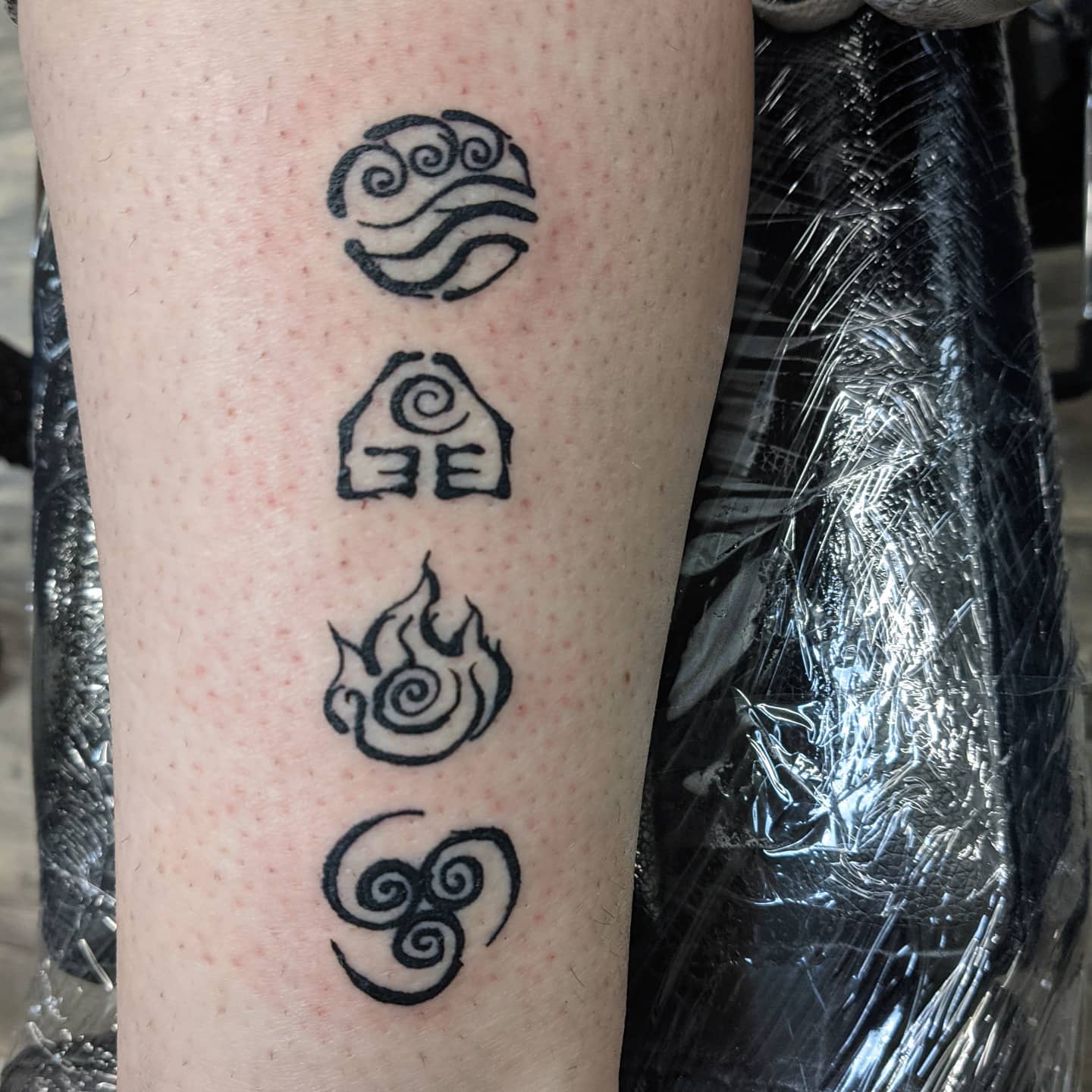 Tattoo of four symbols representing elements on leg: water, earth, fire, and air