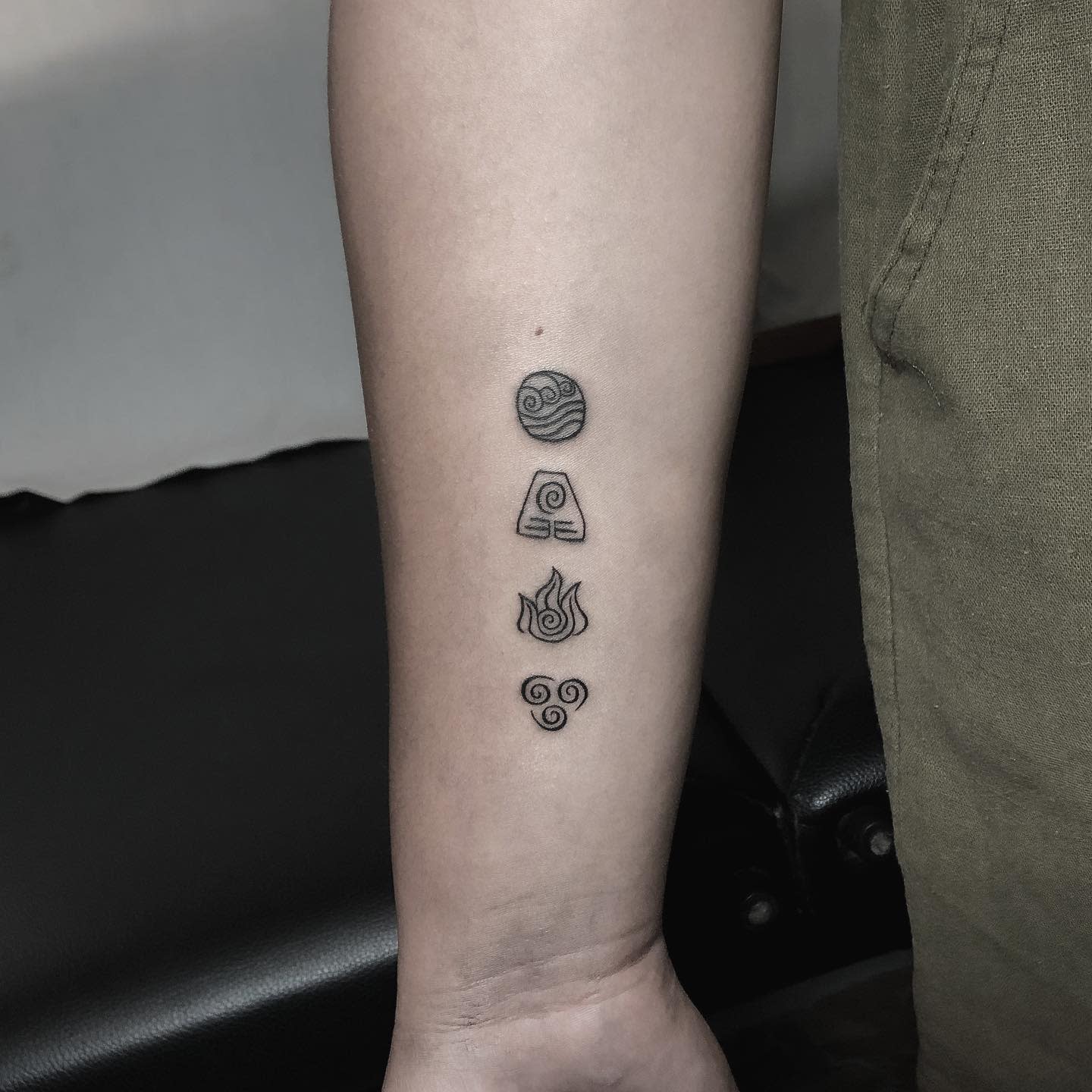 Forearm tattoo featuring vertically aligned symbols of water, earth, fire, and air