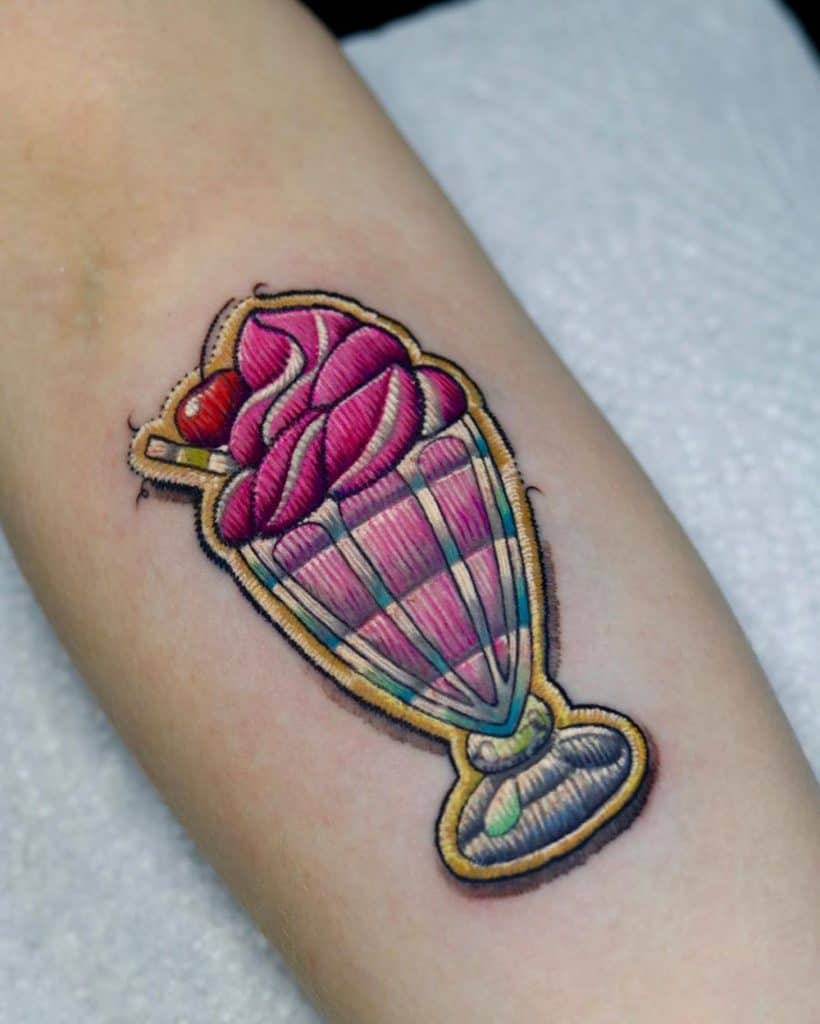 Embroidery-style tattoo of a pink ice cream sundae in a tall glass, featuring detailed stitched textures for a fabric patch effect.