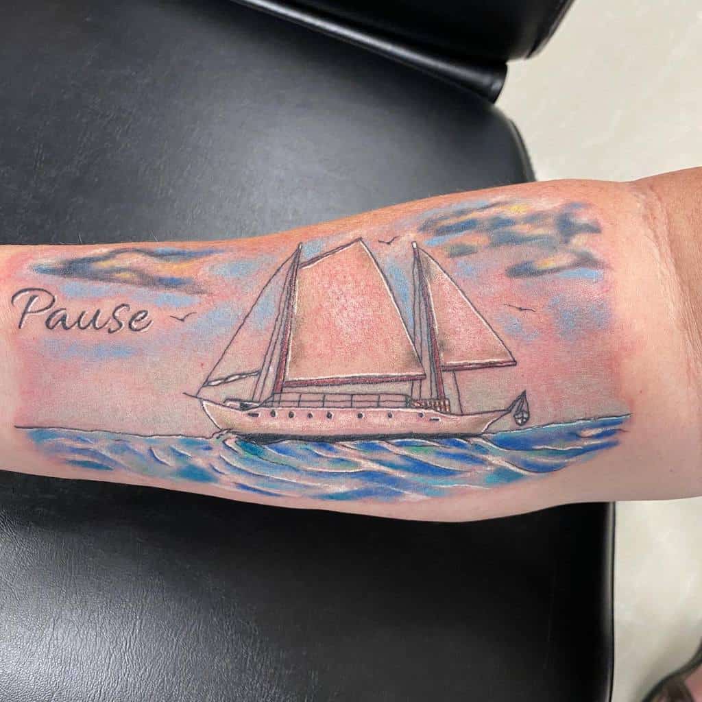 Colorful tattoo of a sailboat on the ocean with a pastel sky, featuring the word 'Pause' in script and birds flying in the background