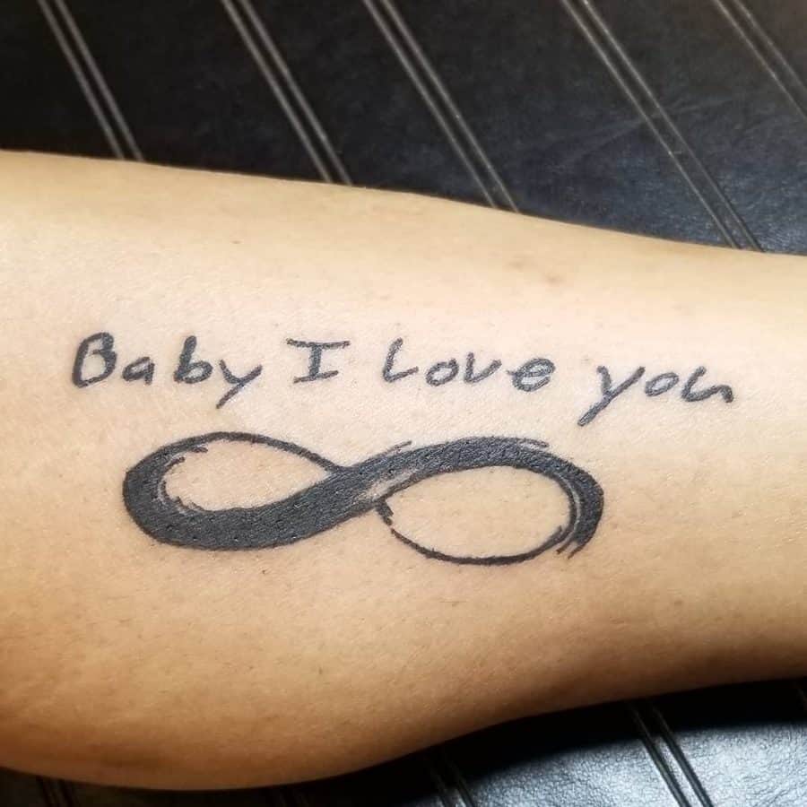This tattoo features the phrase "Baby I love you" written in a casual script above a bold infinity symbol. The infinity symbol, typically representing eternal love and endless connection, complements the message in the text, symbolizing an everlasting bond with a significant other. The use of solid black ink gives the design a clean, classic look, with a personal and emotional touch.