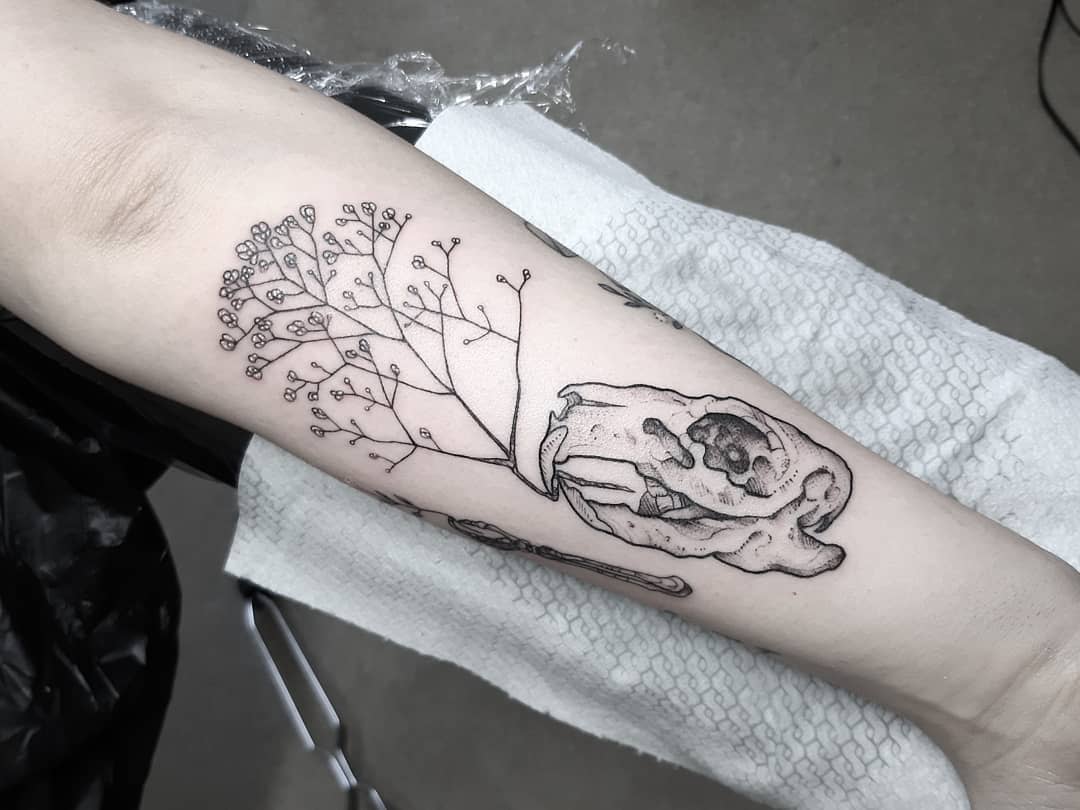 Tattoo on an arm showing a baby's breath flower and an animal skull
