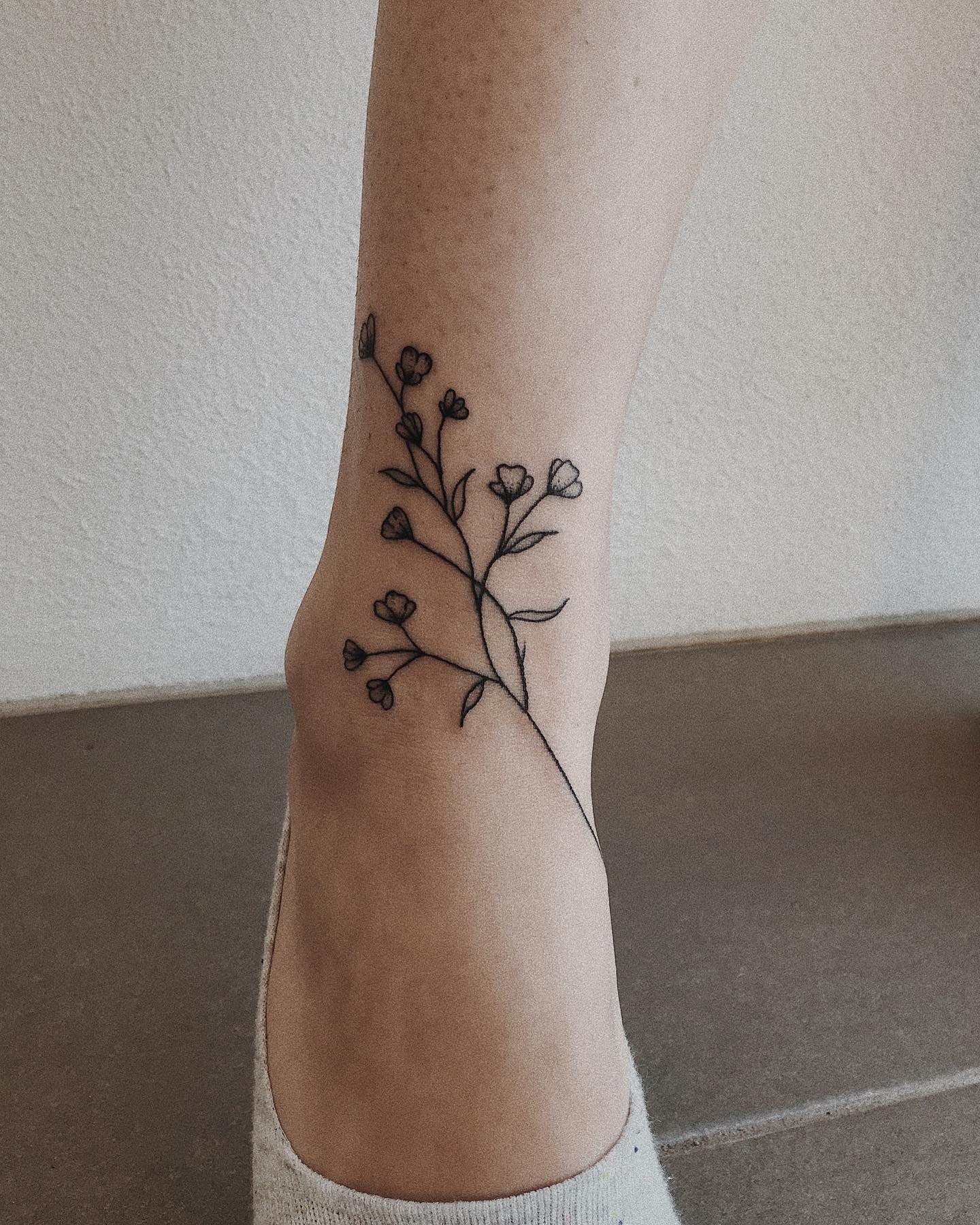 Black ink baby's breath tattoo on the side of an ankle, delicate branches with small flowers