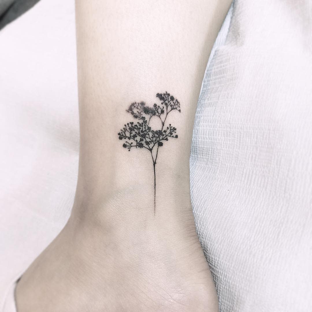 Delicate black ink tattoo of a tree branch with baby's breath on an ankle
