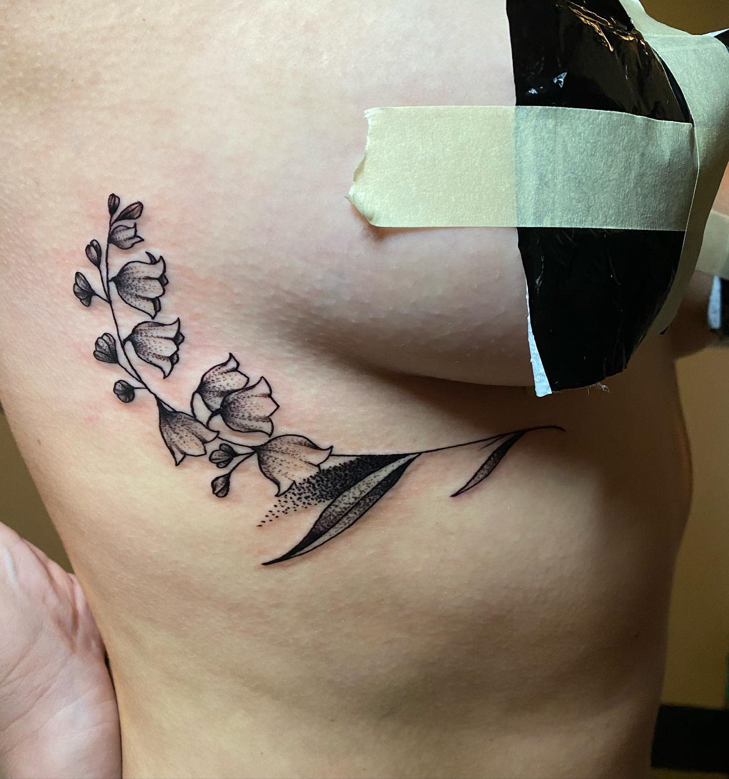Tattoo in progress of baby's breath flowers and leaves on ribcage