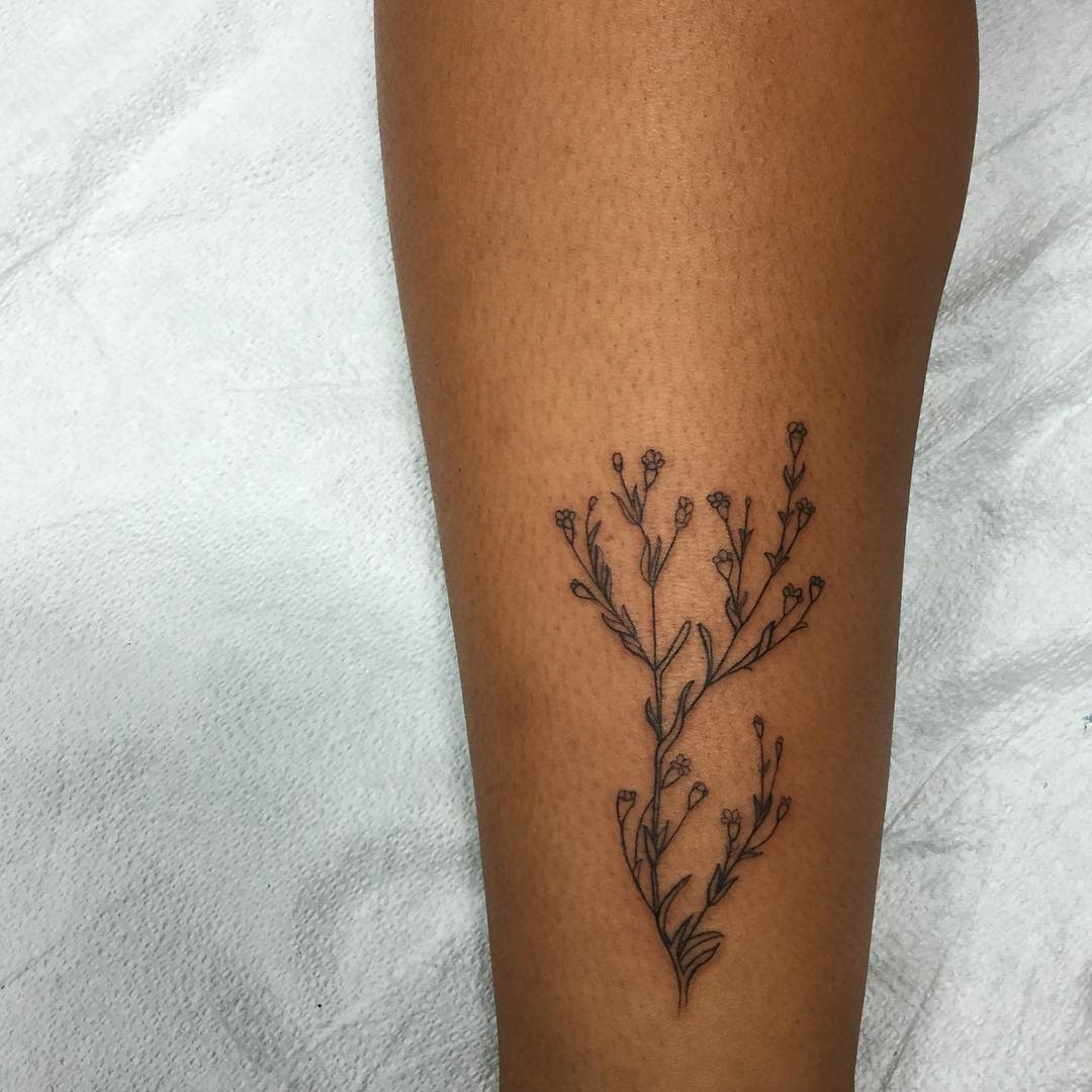 Close-up of a forearm with a delicate black ink tattoo featuring baby's breath branches