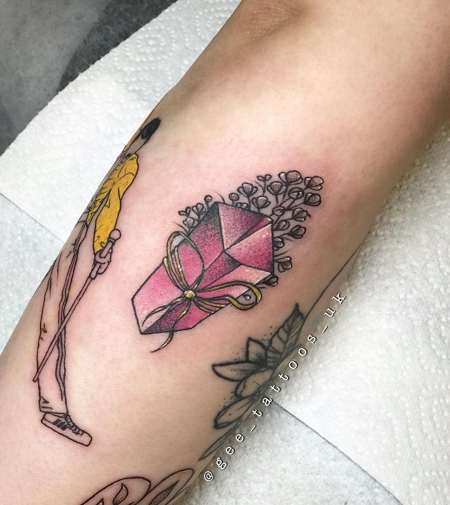 Tattoo depicting flowers and a gift box beside a figure on the forearm