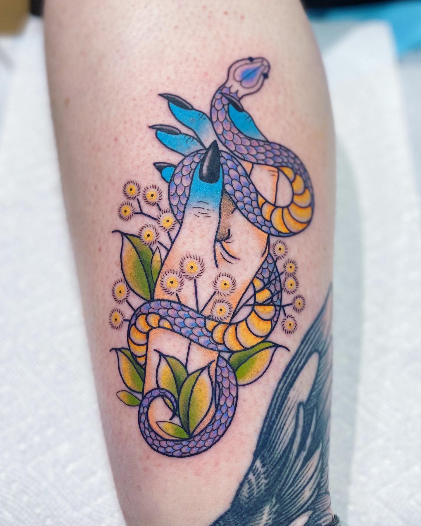 Tattoo of a snake wrapped around fingers with flowers and leaves on an arm