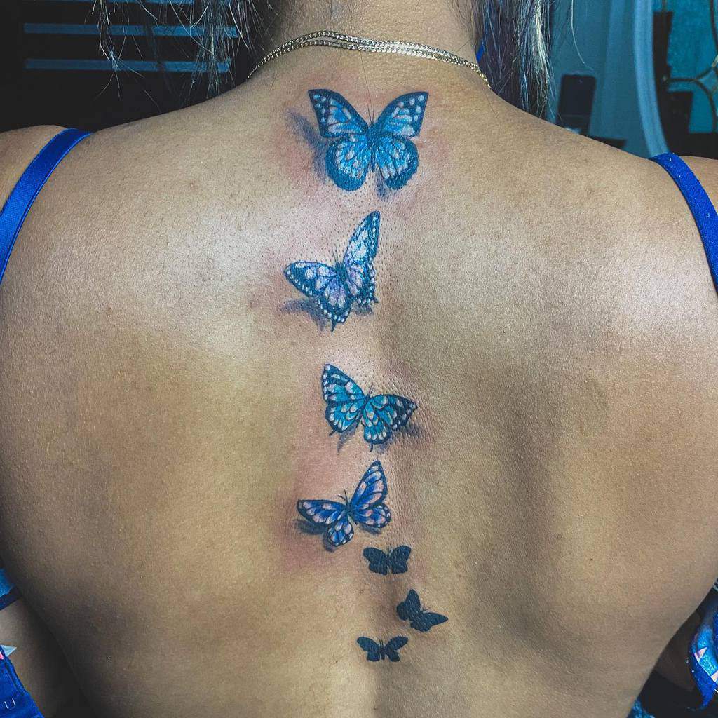 Back tattoo featuring a stunning vertical line of blue butterflies, each increasingly smaller from top to bottom