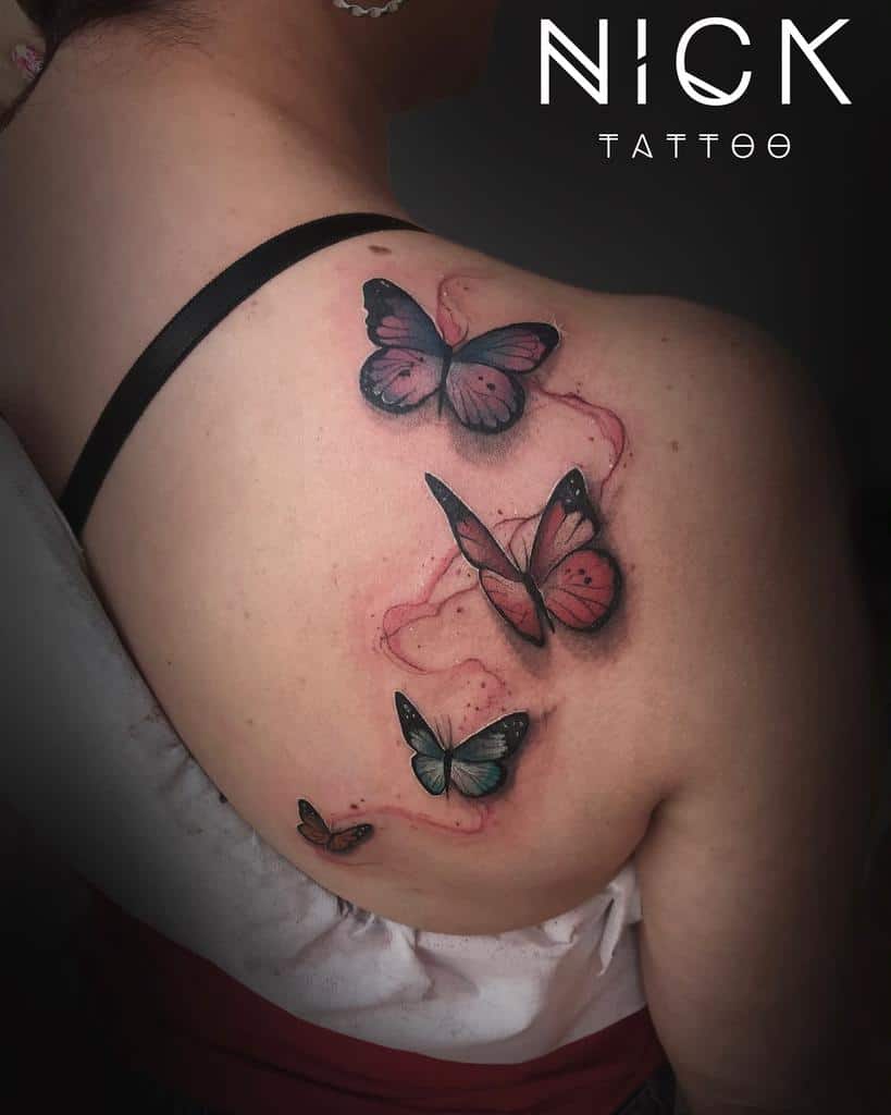 A shoulder tattoo featuring three colorful butterflies in flight with a background of pink shading