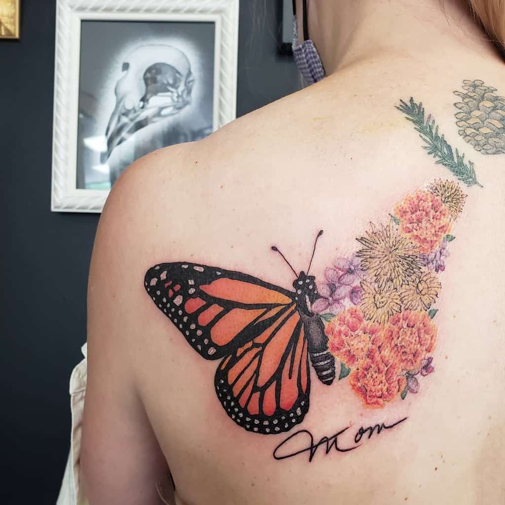 Woman's shoulder tattoo of a monarch butterfly and flowers with "Mom" written beneath