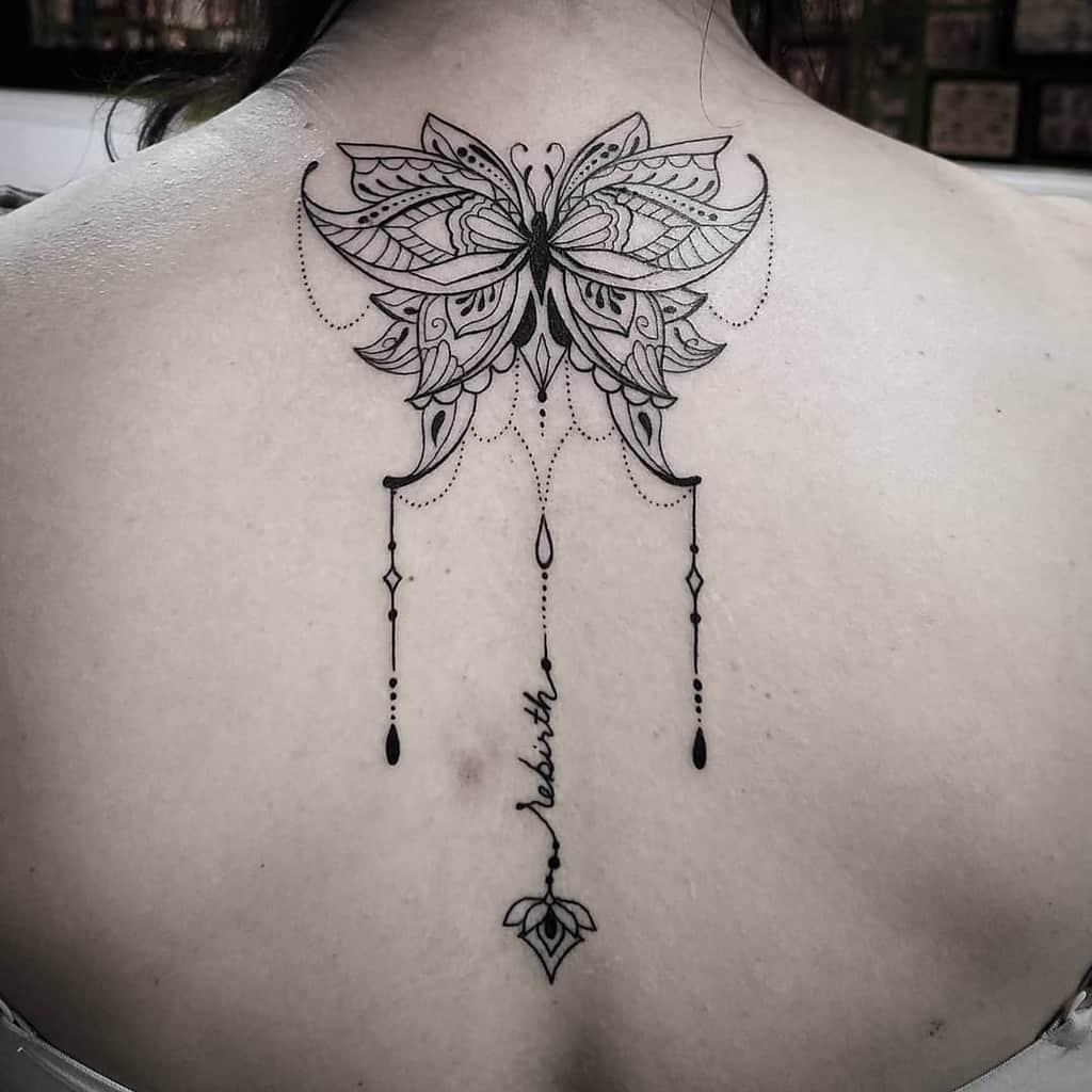 Elegant black ink tattoo featuring a detailed butterfly with chandelier-style drops and the word 'rebirth' written vertically connected to a central leaf motif