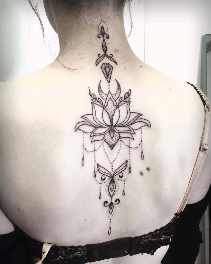 Elegant black ink back tattoo featuring a lotus flower with a crescent moon, chandelier-style beadwork, a butterfly, and geometric details