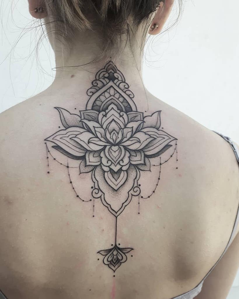 Black ink back tattoo featuring a large symmetrical lotus flower with intricate mandala details, chandelier-style beads, and ornamental extensions along the spine