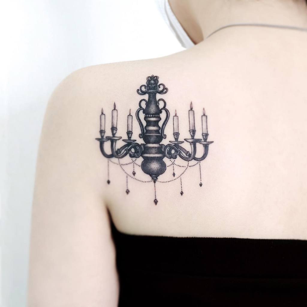 Elegant black ink tattoo featuring a detailed chandelier with six candles and delicate hanging beads, designed in a vintage gothic style