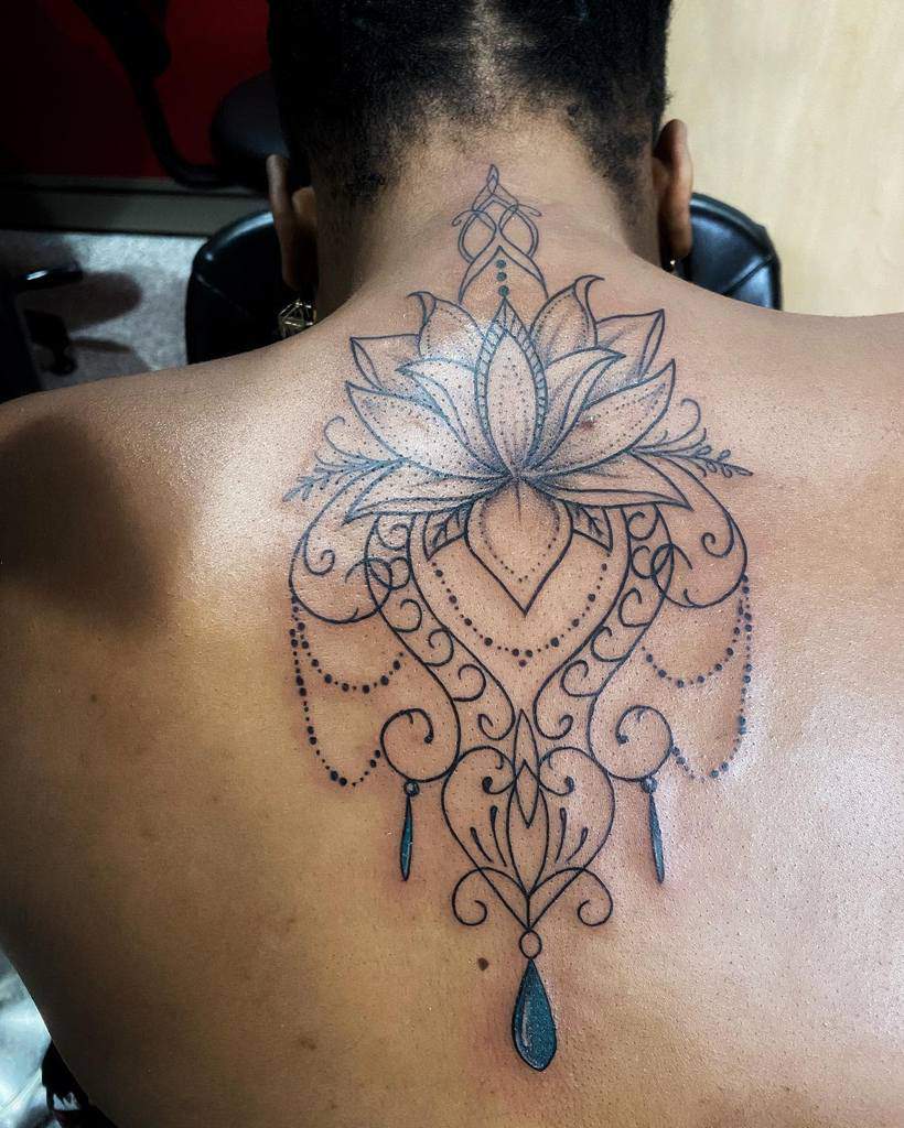 Black ink back tattoo featuring a large lotus flower with intricate mandala details, chandelier-style beads, and blue teardrop accents