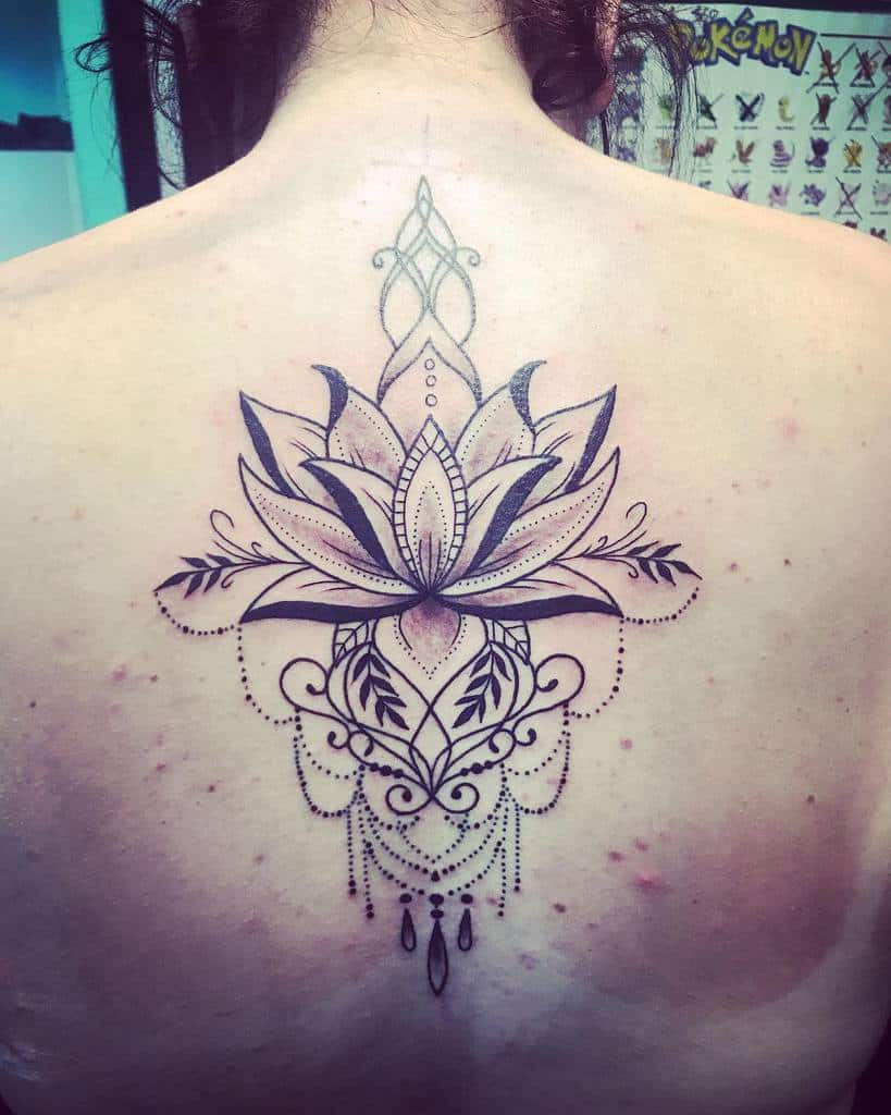 Elegant black ink back tattoo featuring a large lotus flower with mandala-style details, delicate chandelier beads, and ornamental flourishes 