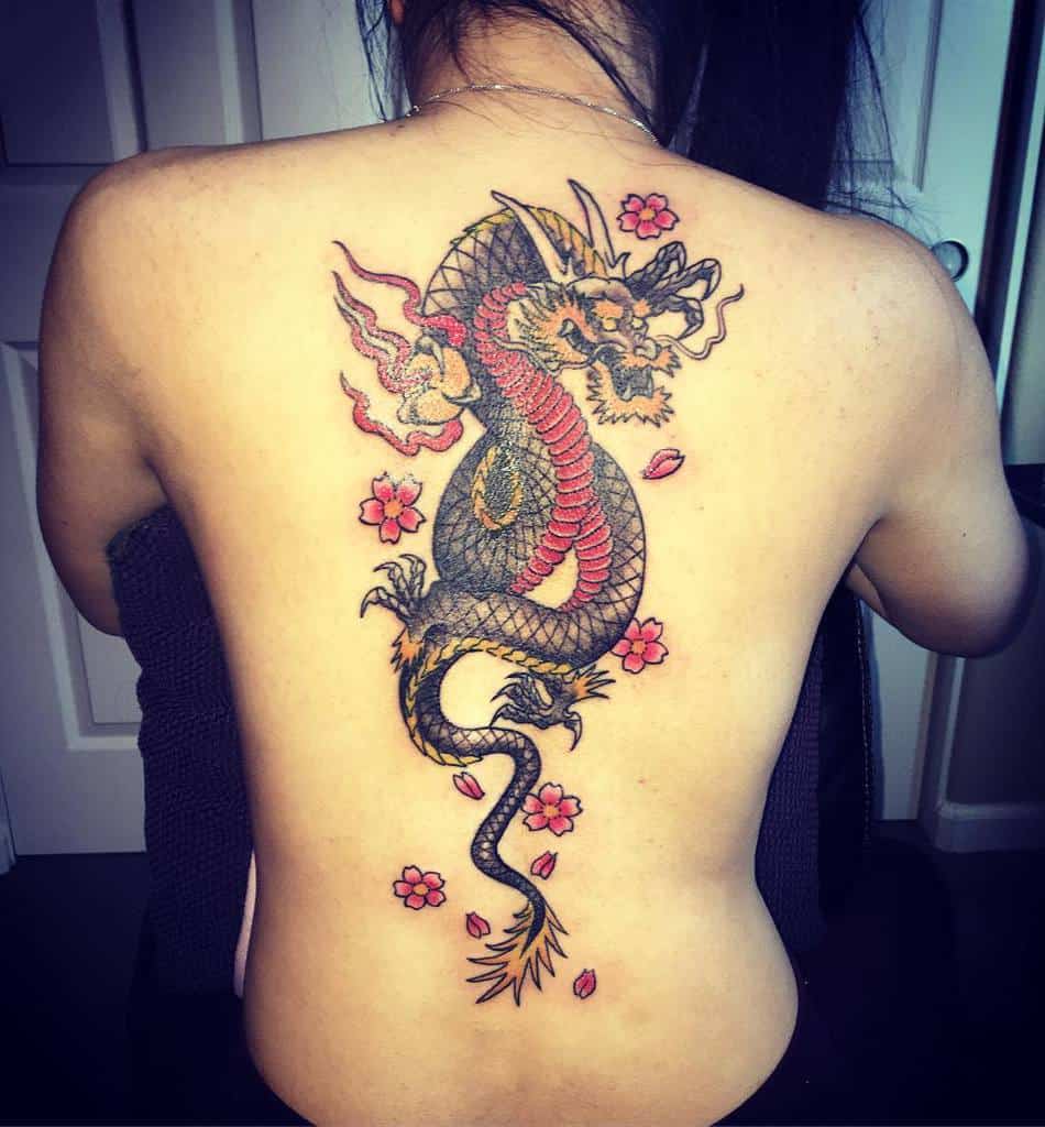A woman with a colorful dragon tattoo on her back, surrounded by pink flowers