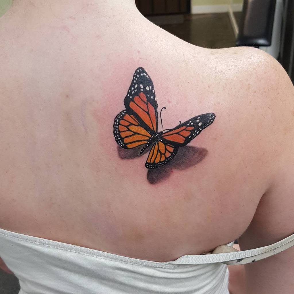 Monarch butterfly tattoo on upper back, showcasing vibrant orange and black wings with delicate white spots