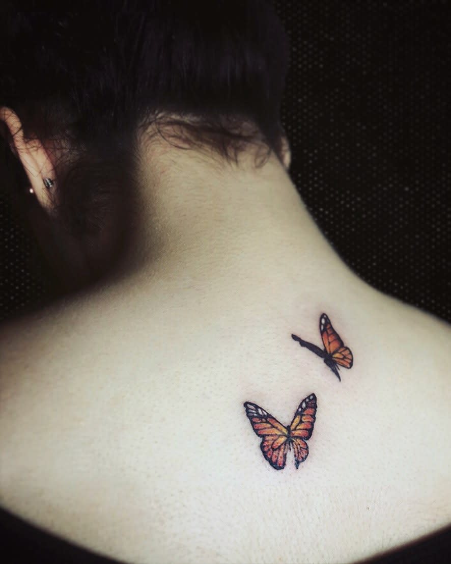 Two monarch butterfly tattoos, vibrant in orange and black, grace the back of a person's upper back