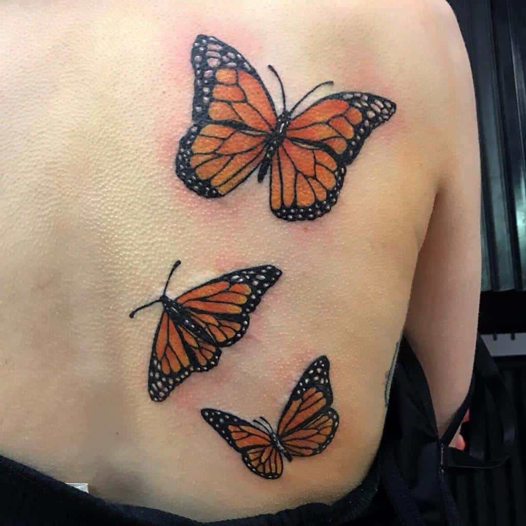 Three vibrant monarch butterflies, with their striking orange and black wings, are beautifully tattooed on a back