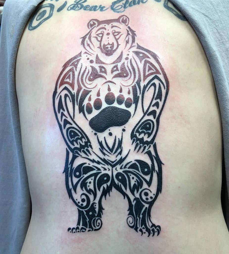 A stunning tattoo of a stylized bear adorned with intricate tribal patterns spans across the person's back, its artistic flair highlighted with shoulders beautifully visible
