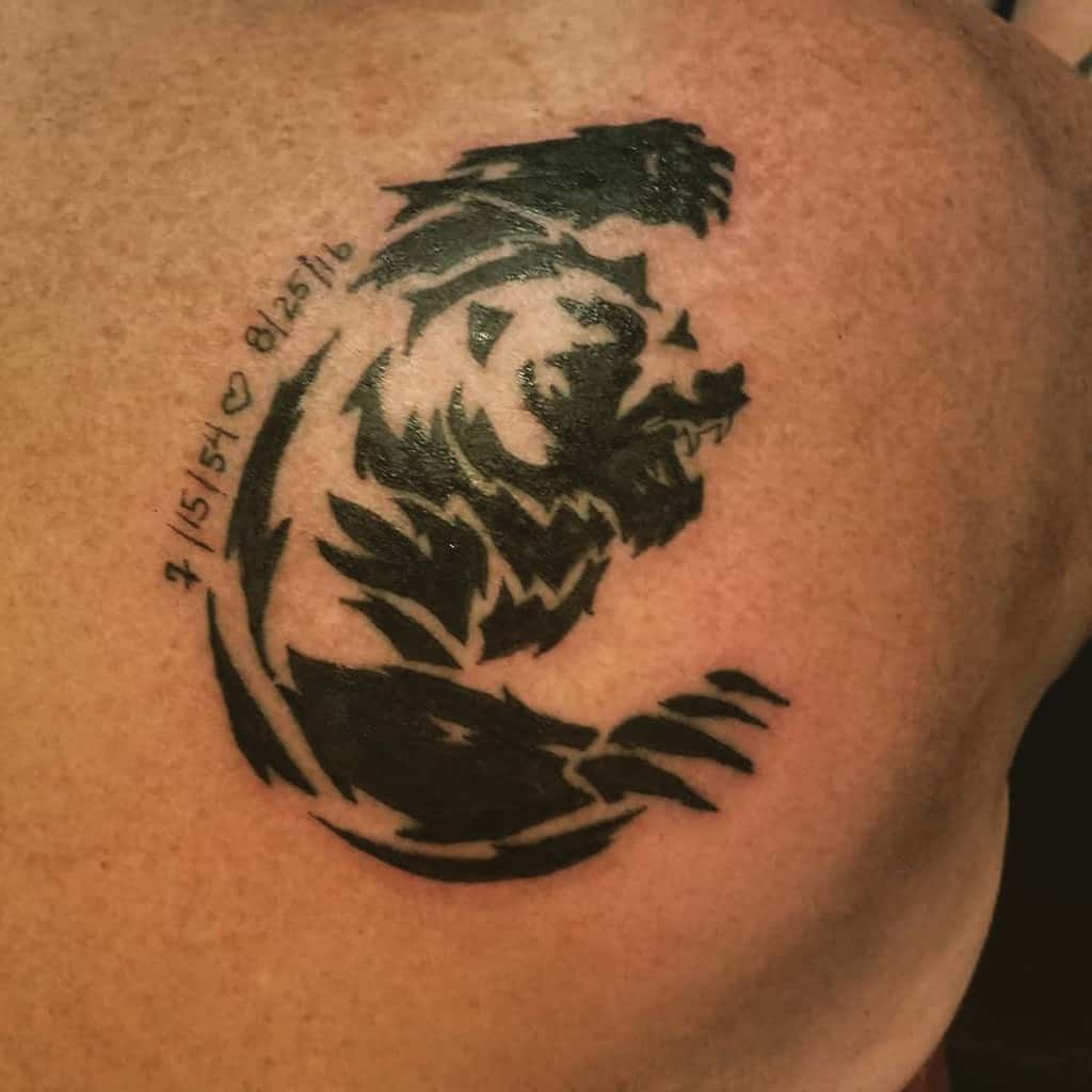A striking black tribal-style tattoo of a bear adorns the shoulder, featuring two meaningful dates against a tan skin backdrop