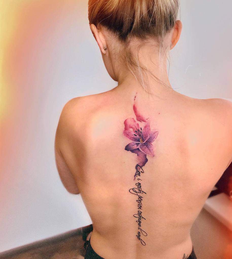 Elegant watercolor-style tattoo of a pink lily with flowing script reading 'Con i nostri bensieri costruiama il marglo,'