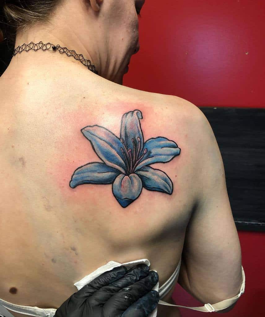Bold tattoo of a vibrant blue lily with black outlines and shading, symbolizing tranquility, renewal, and personal growth