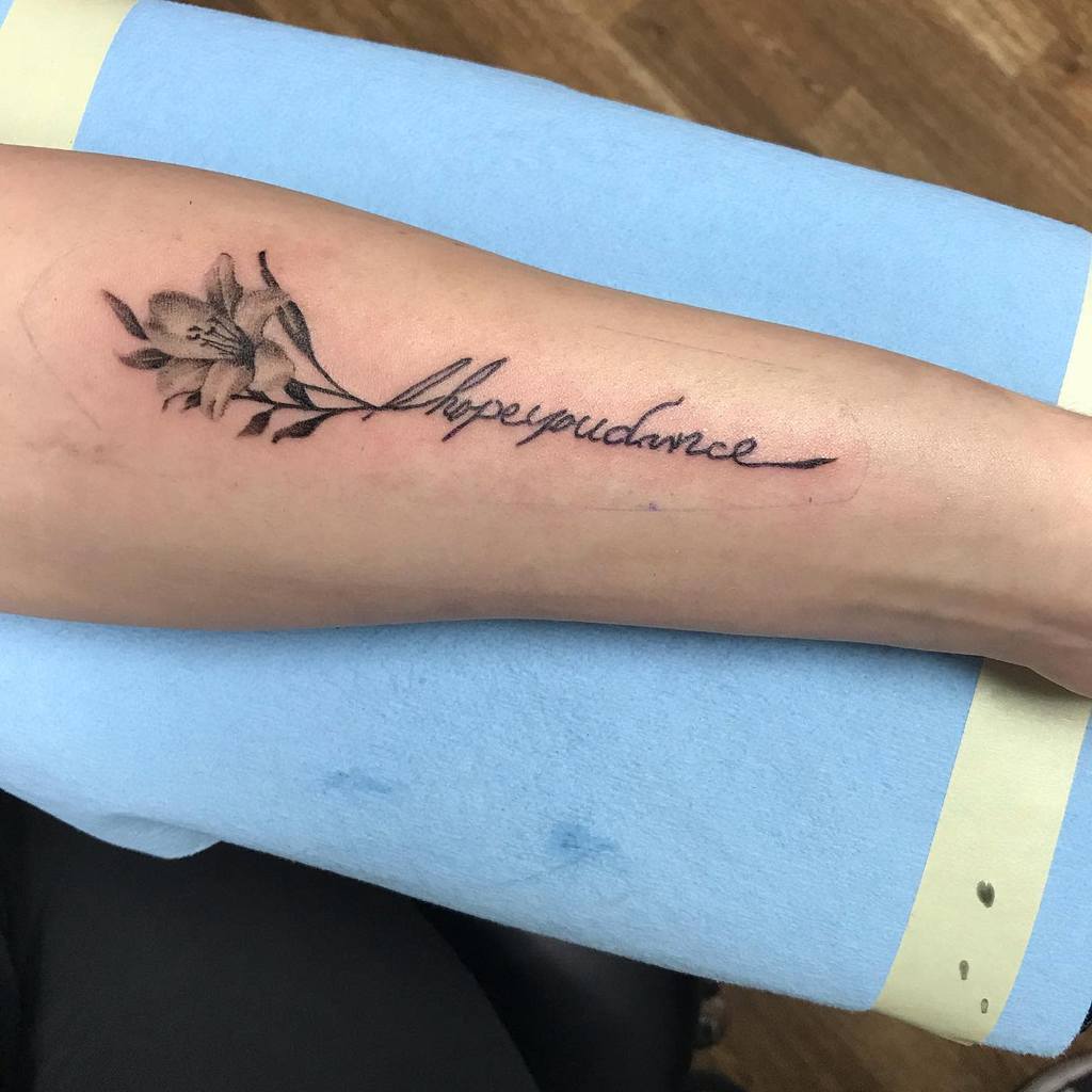 Elegant tattoo featuring a delicate lily with cursive script that reads 'I hope you dance,' symbolizing growth, resilience, and inspiration
