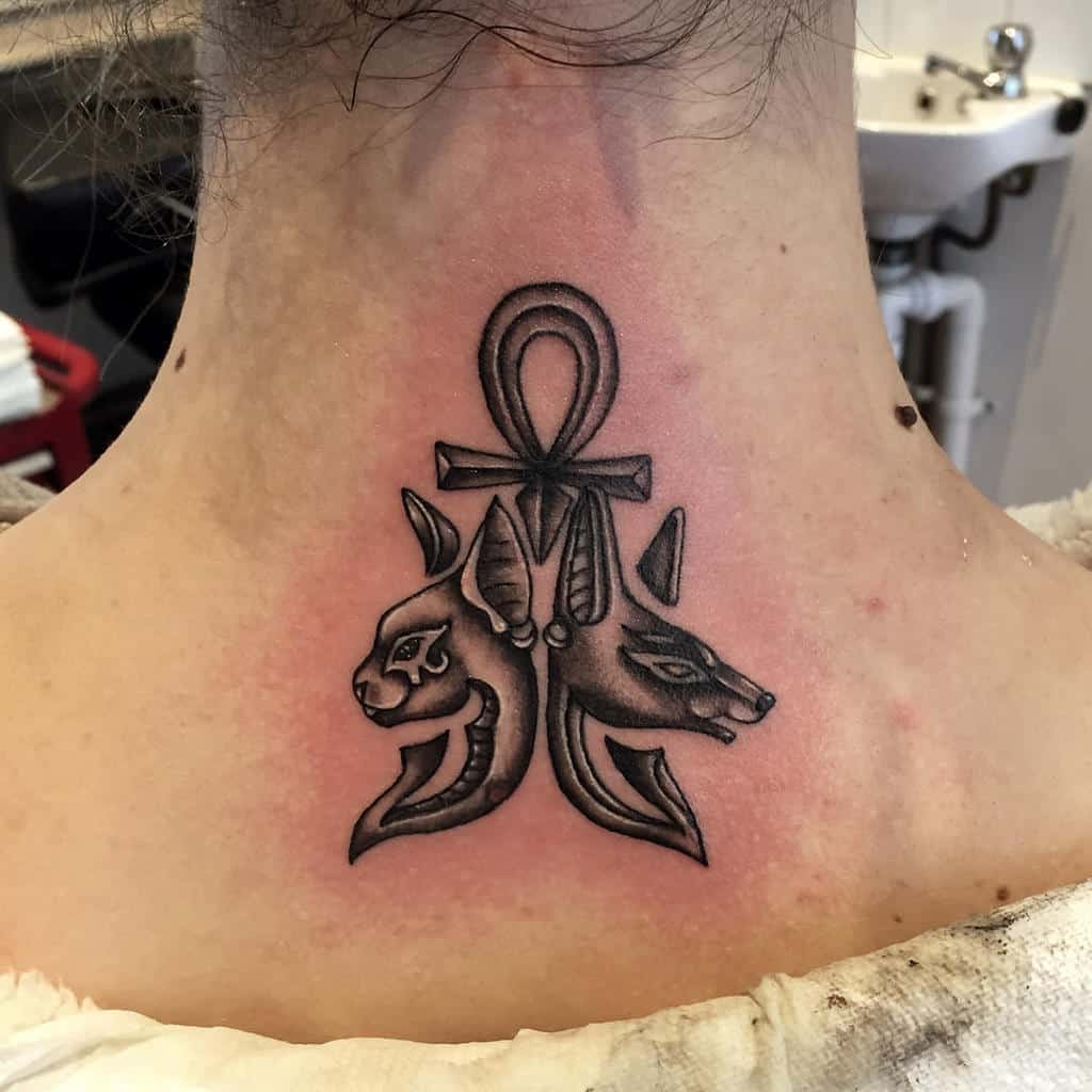 Tattoo of an ankh with a cat and a jackal head on the back of neck