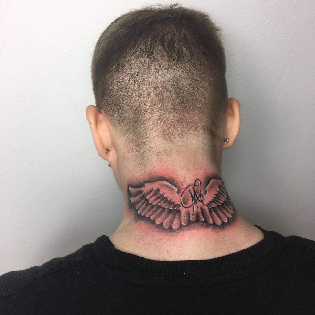 Tattoo of wings and a signature or initials gracefully inked on the back of neck against a pristine white wall