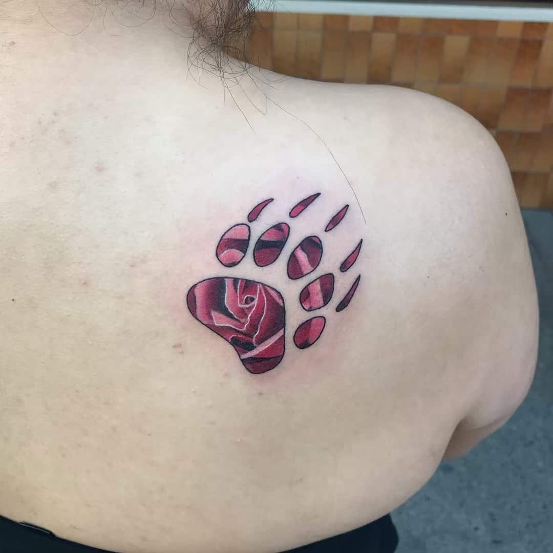 Tattoo of a bear paw with a vibrant red rose in the center, on the upper back
