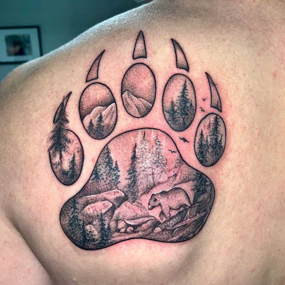 A bear paw tattoo with trees, mountains, and a bear on a person's back