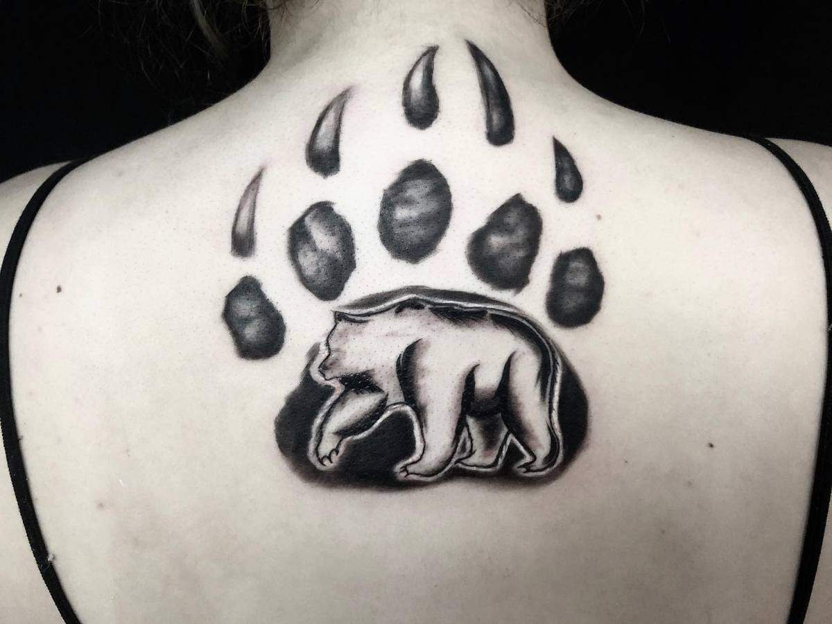Tattoo of a bear in a bear paw print design on the upper back of a person