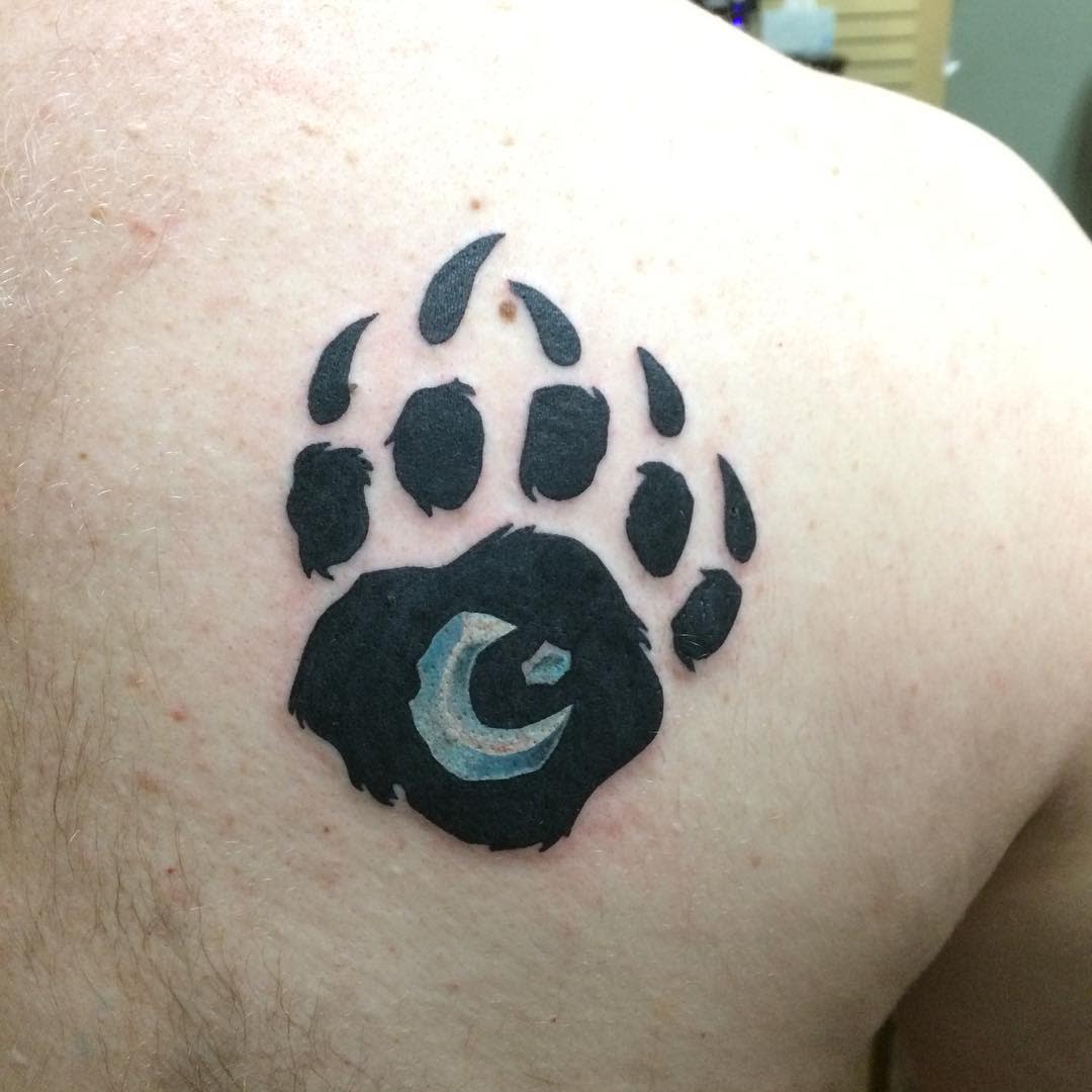 Tattoo of a bear paw print with a small crescent moon in the center on a person's back