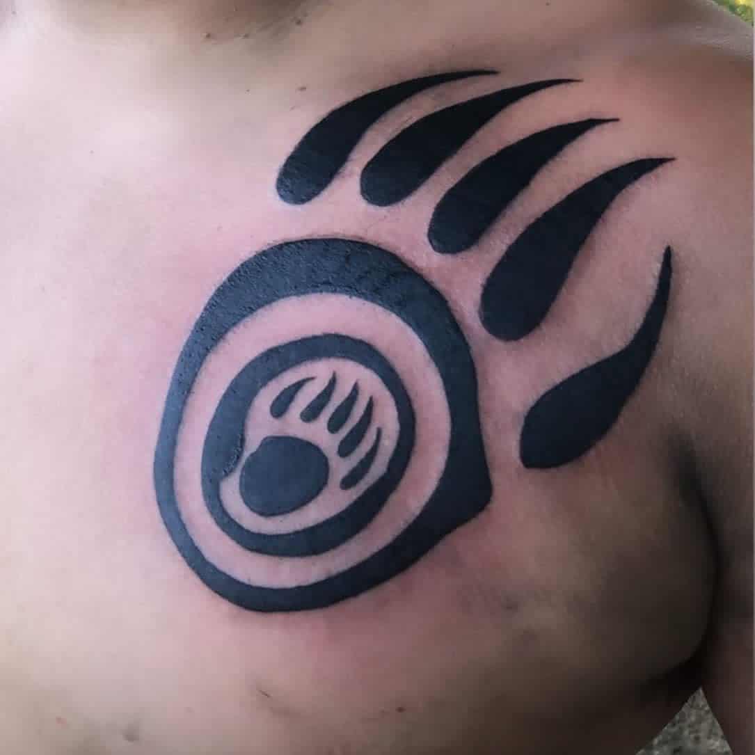 Black bear paw tattoo with an intricate design on a person’s upper chest, featuring a stunning bear paw motif