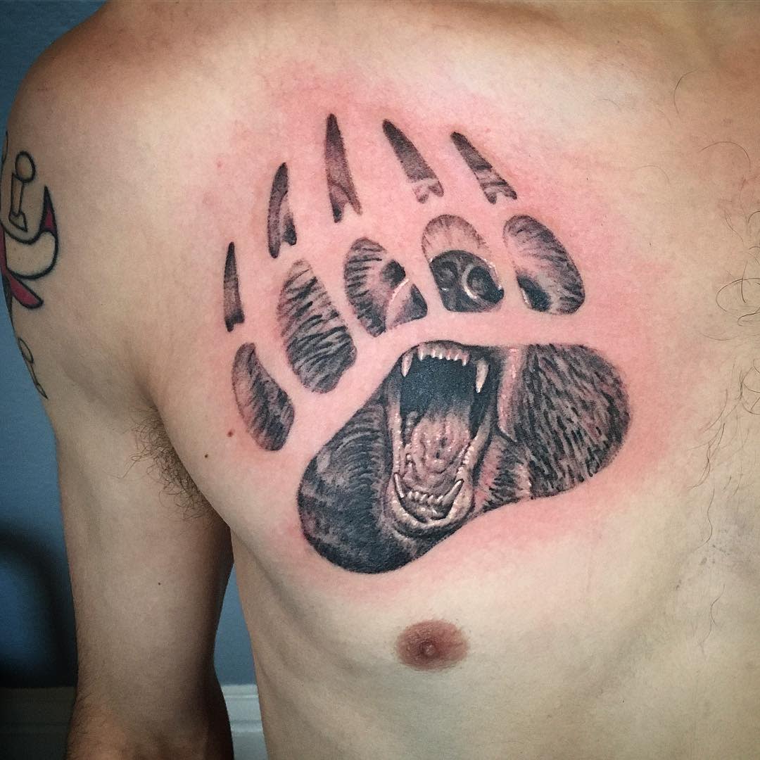 Roaring bear with face inside a detailed bear paw tattoo on the left chest